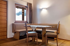 A cozy room with a wooden bench, a table, and chairs, a window with curtains, and a wall-mounted light fixture.