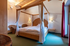 A four-poster bed with a canopy, a wicker chair, a nightstand, and wall-mounted lights.