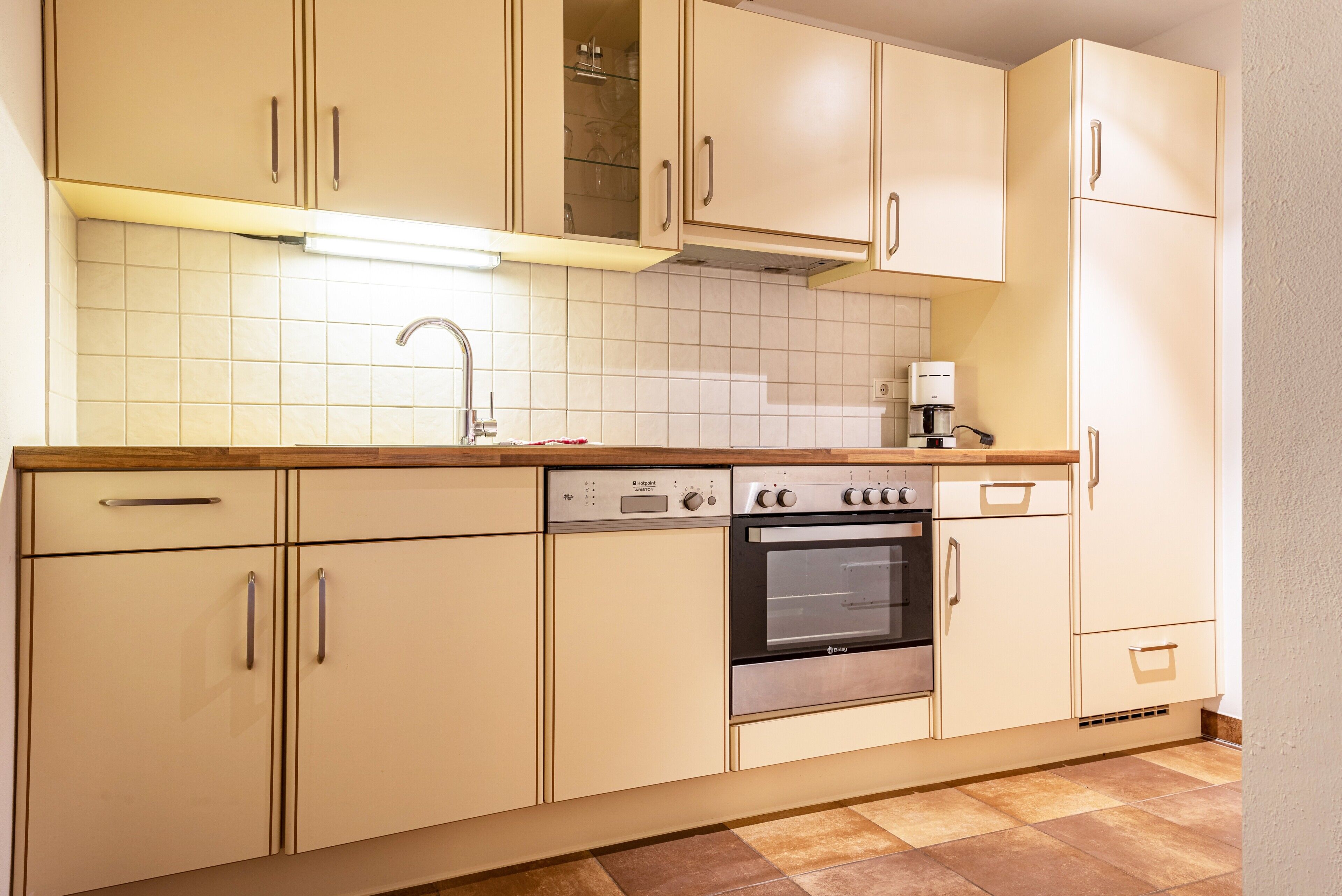 A kitchen with beige cabinets, a stainless steel oven, a coffee maker, and a tiled backsplash.