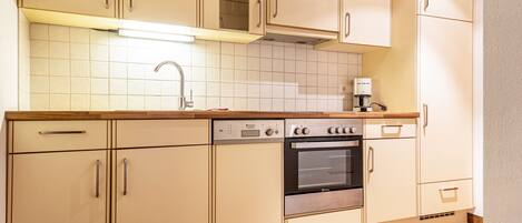 A kitchen with beige cabinets, a stainless steel oven, a coffee maker, and a tiled backsplash.