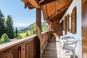 A wooden balcony with a table and chairs, overlooking a mountainous landscape.