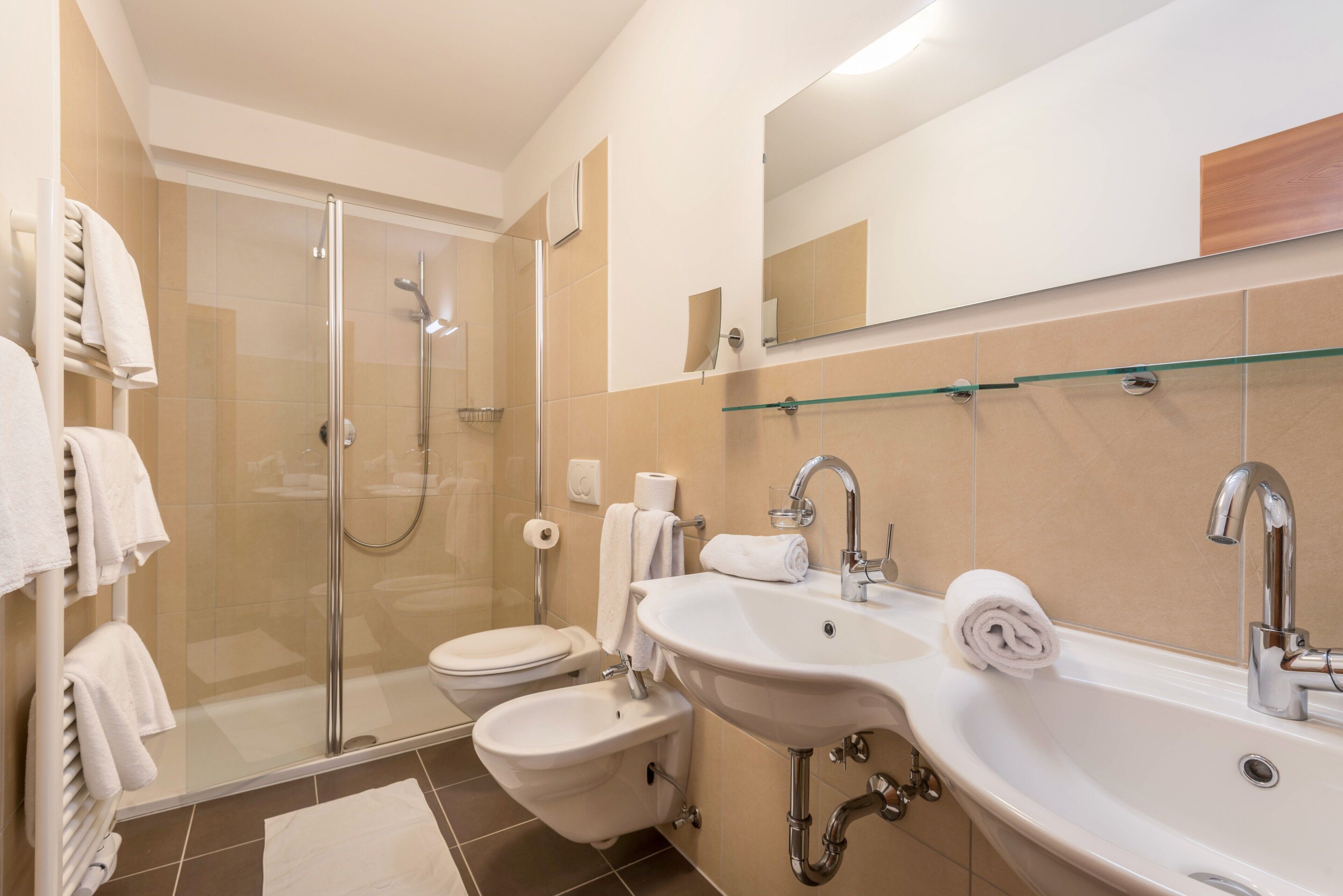 Une salle de bain moderne avec une douche à parois de verre, deux lavabos, des toilettes et un miroir.