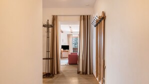 Un couloir avec un tapis à rayures, un plancher en bois et une vue sur une pièce où l’on aperçoit un fauteuil rouge et un téléviseur.
