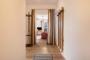 Un couloir avec un tapis à rayures, un plancher en bois et une vue sur une pièce où l’on aperçoit un fauteuil rouge et un téléviseur.