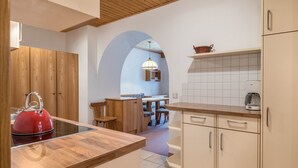 A kitchen with wooden cabinets, a red kettle, a tiled backsplash, and a dining area with a table and chairs.
