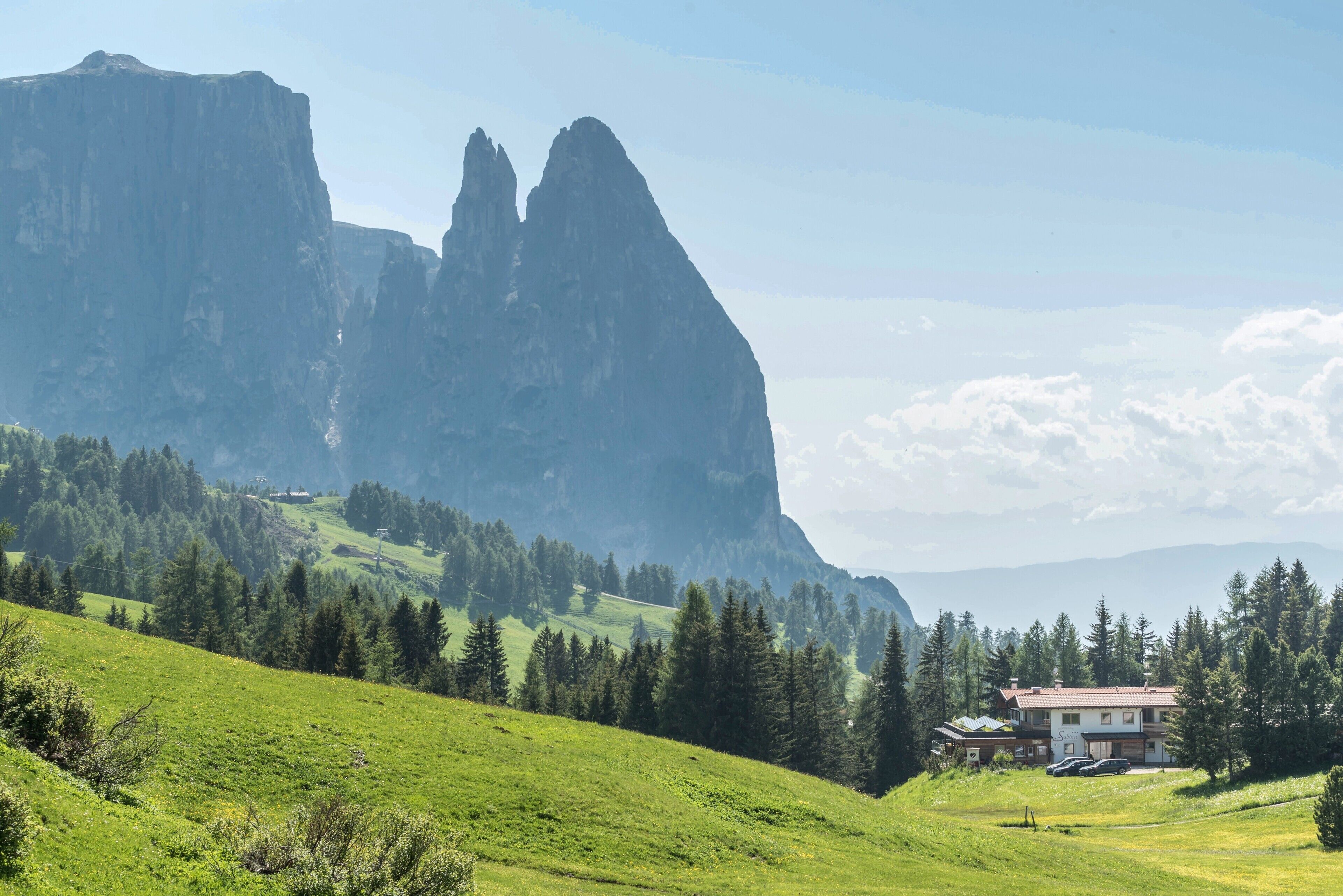 A mountain landscape with a building featuring a red roof and white walls, surrounded by greenery and trees.