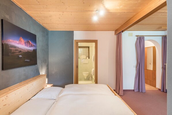 Ein Schlafzimmer mit Holzboden, einem Bett, einem Gemälde und einem durch eine offene Tür einsehbaren Badezimmer.