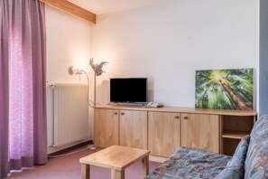 Une pièce comprenant un meuble en bois, un téléviseur posé dessus, un tableau accroché au mur, une petite table et un canapé.
