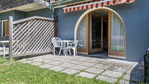 Un bâtiment doté d’un balcon en bois, d’un espace extérieur abrité avec des chaises, et d’une porte avec un panneau de verre.