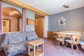 Une pièce chaleureuse avec un canapé à motifs, une table et des chaises en bois, un buffet en bois et un tableau représentant un cerf accroché au mur.