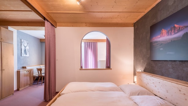 Une chambre à coucher avec une tête de lit en bois, un lit avec une literie blanche, une fenêtre avec des rideaux, un bureau avec une chaise et un tableau accroché au mur.