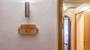 Une enseigne en bois portant l’inscription « Euringer N-2 », fixée sur un mur blanc, avec une porte et un couloir.
