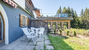 Una casa moderna con un patio, mobiliario exterior y vistas al bosque circundante.