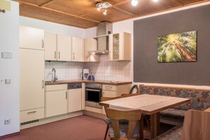 Une cuisine compacte avec des meubles blancs, un four encastré et un coin repas comprenant une banquette et une table.