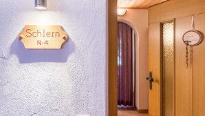 Un letrero de madera con 'Schlern N-4' sobre una pared texturizada, una puerta de madera con un detalle circular y una ventana que deja ver parte de una habitación con cortina.