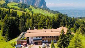 A hotel with a red-tiled roof, solar panels, a dining area with outdoor seating, and a view of mountains. - Holiday Apartment "Ferienparadies Sabina Piz" in the Nature Park Next to Seiser Alm (Castelrotto / Alpe di Siusi)