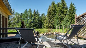 Two outdoor chairs facing a small pond with a wooden deck and a building in the background. - Holiday Apartment "Ferienparadies Sabina Piz" in the Nature Park Next to Seiser Alm (Castelrotto / Alpe di Siusi)
