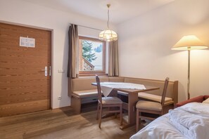 Une pièce avec une porte en bois, une fenêtre avec des rideaux, une table avec des chaises, un lit et un lampadaire.