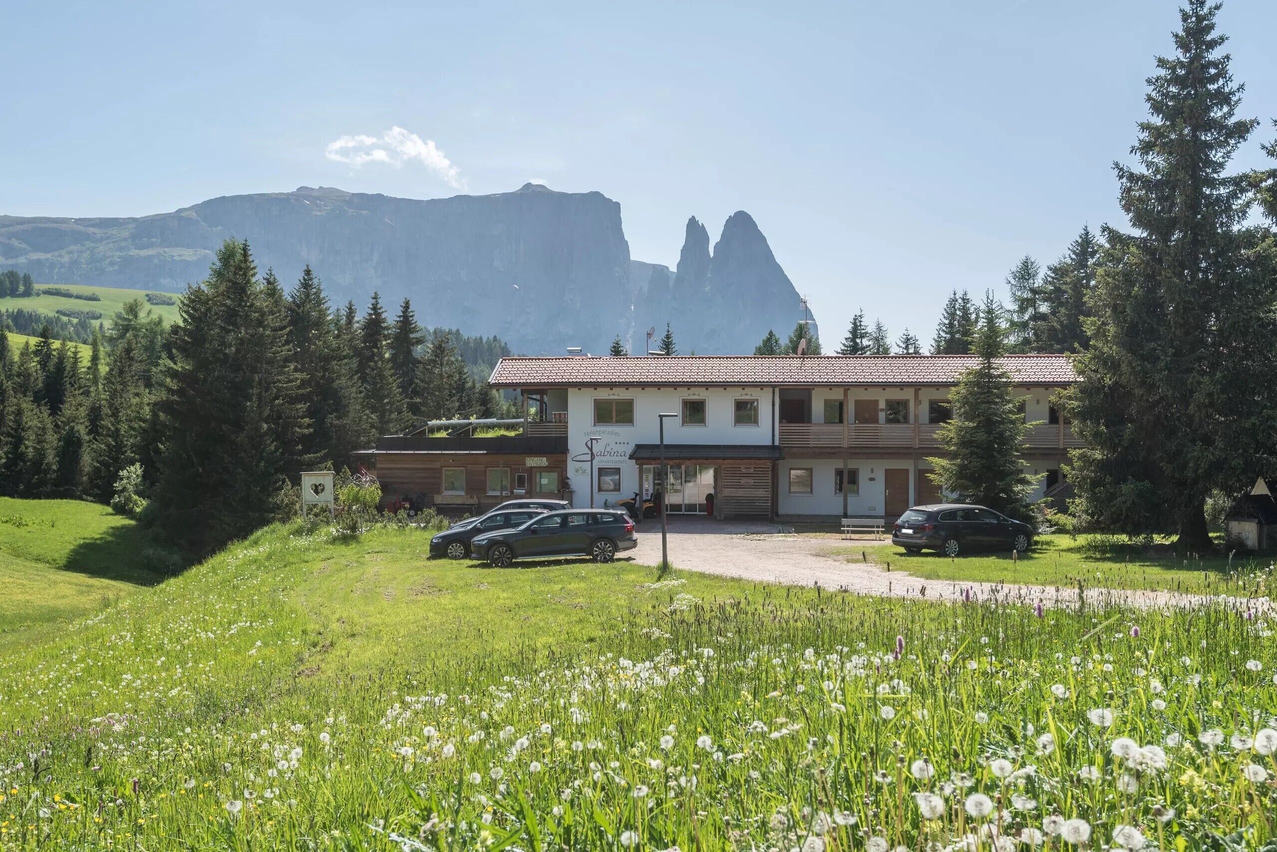 Un hotel con tejado de tejas rojas, un letrero y dos coches estacionados adelante.