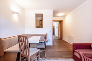 Ein Essbereich mit Holztisch und -stühlen, einem roten Sofa und einem Flur, der in eine Küche führt.