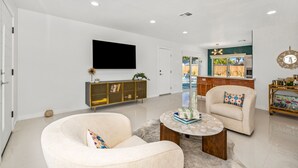 Una sala de estar moderna con una televisión de pantalla plana, un mueble de madera, dos sillones y una mesa de centro.