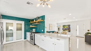 Una cocina moderna con armarios blancos, una isla central y salpicadero color turquesa.