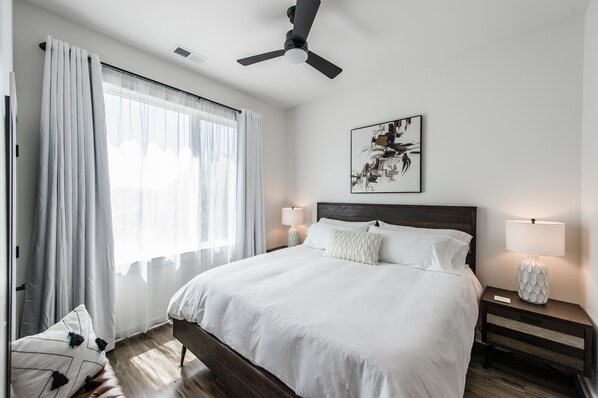 A neatly arranged bedroom with a large bed, two bedside tables with lamps, a ceiling fan, and a window with sheer curtains. - Modern & Stylish Townhome with Cozy Rooftop (Nashville)