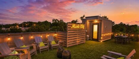 An outdoor seating area with lounge chairs and a neon sign reading 'Music City' against a twilight sky.