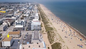Vue aérienne d’une ville côtière avec une longue plage bordée d’immeubles et de voitures garées.