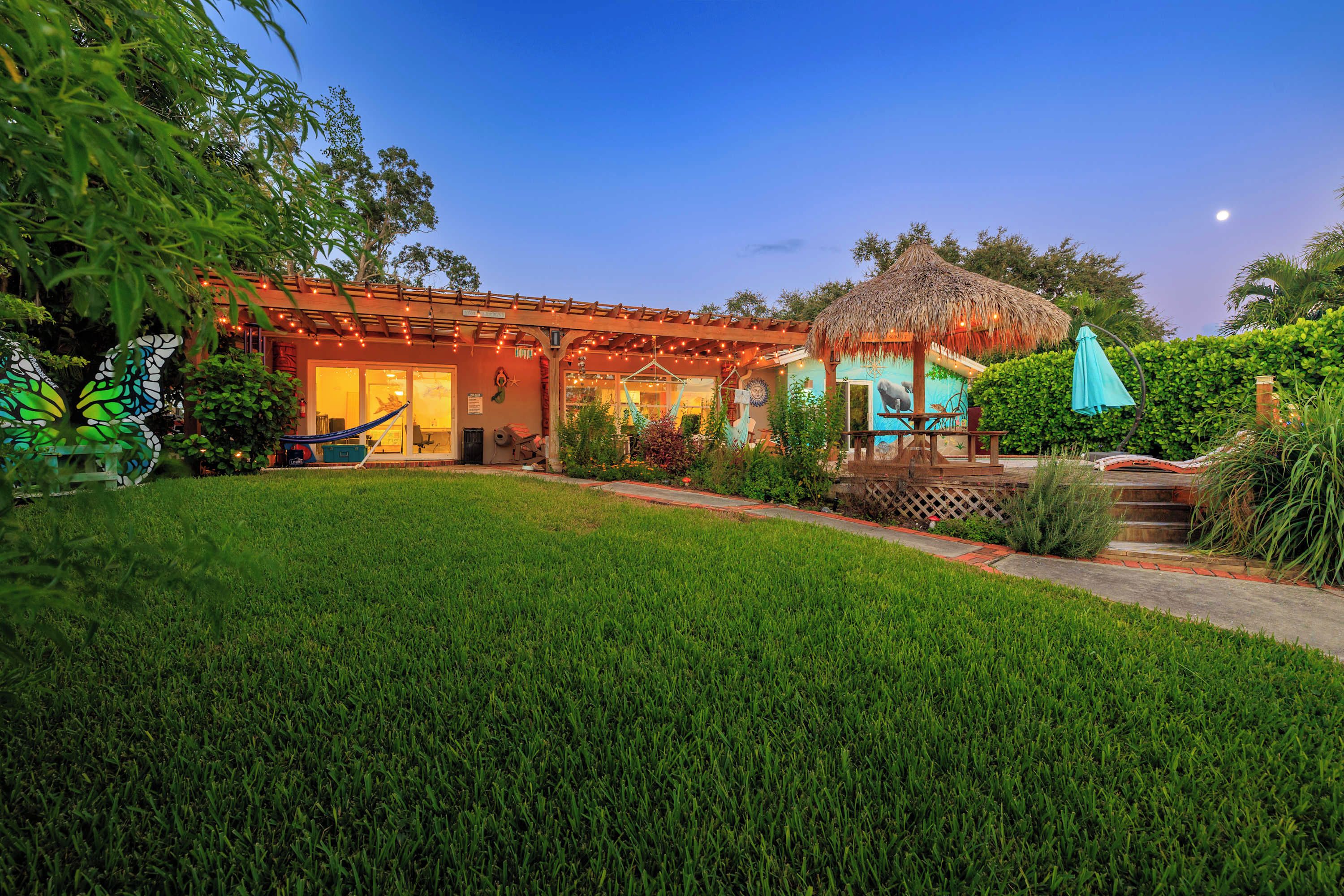 A house with a covered patio, a hammock, and a thatched-roof structure.