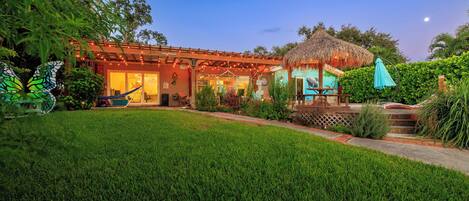 A house with a covered patio, a hammock, and a thatched-roof structure.