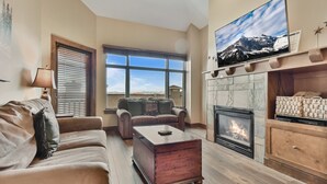 Una sala de estar con chimenea, un televisor grande montado encima, un sofá y una mesa de centro.
