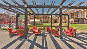 Un área de estar al aire libre con mesas y sillas de madera, una estructura de pérgola y vistas a un edificio con un letrero que dice "Park City Canyons Village".