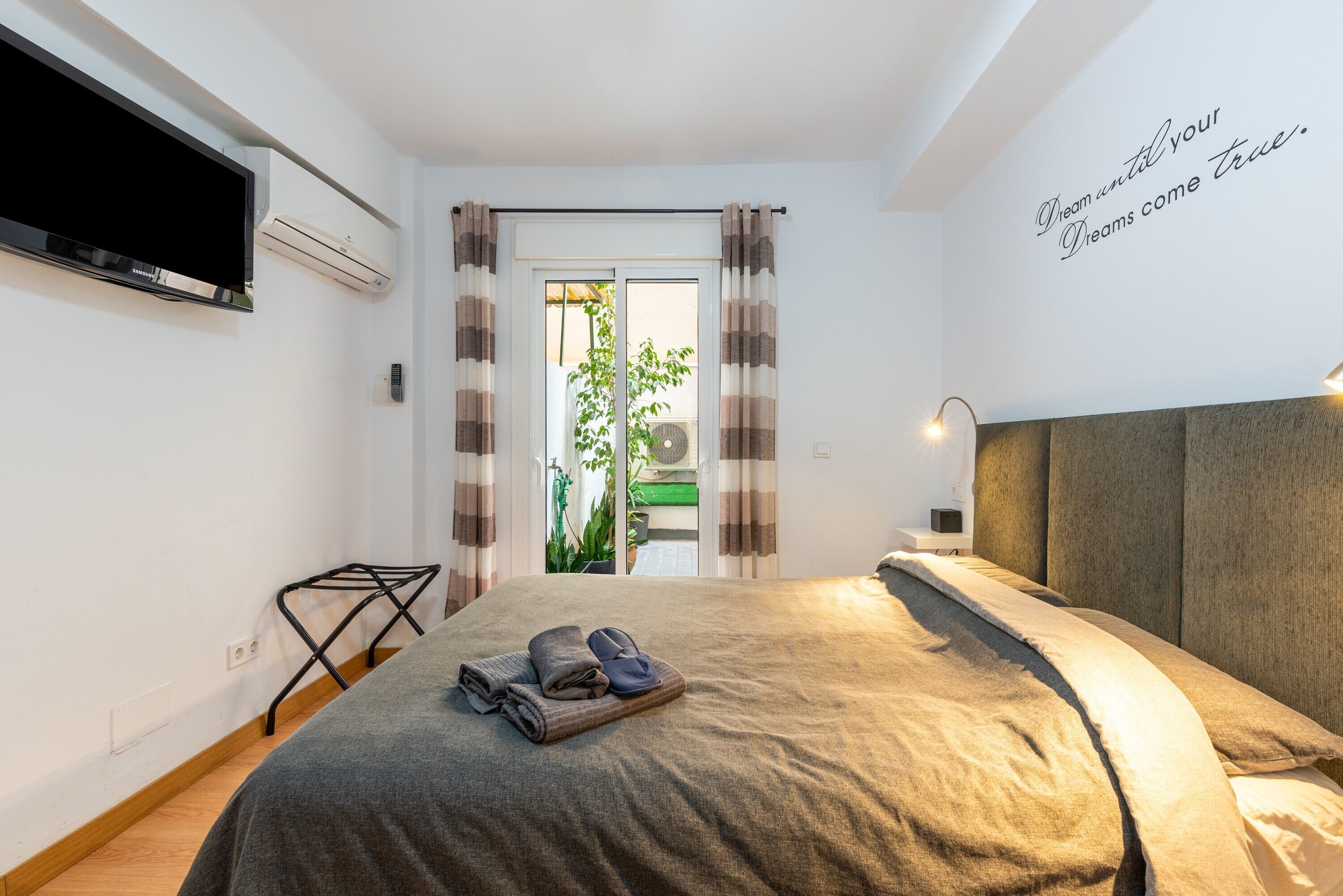Een slaapkamer met een bed, een televisie, een airconditioner, een wandlamp en een inspirerende quote.