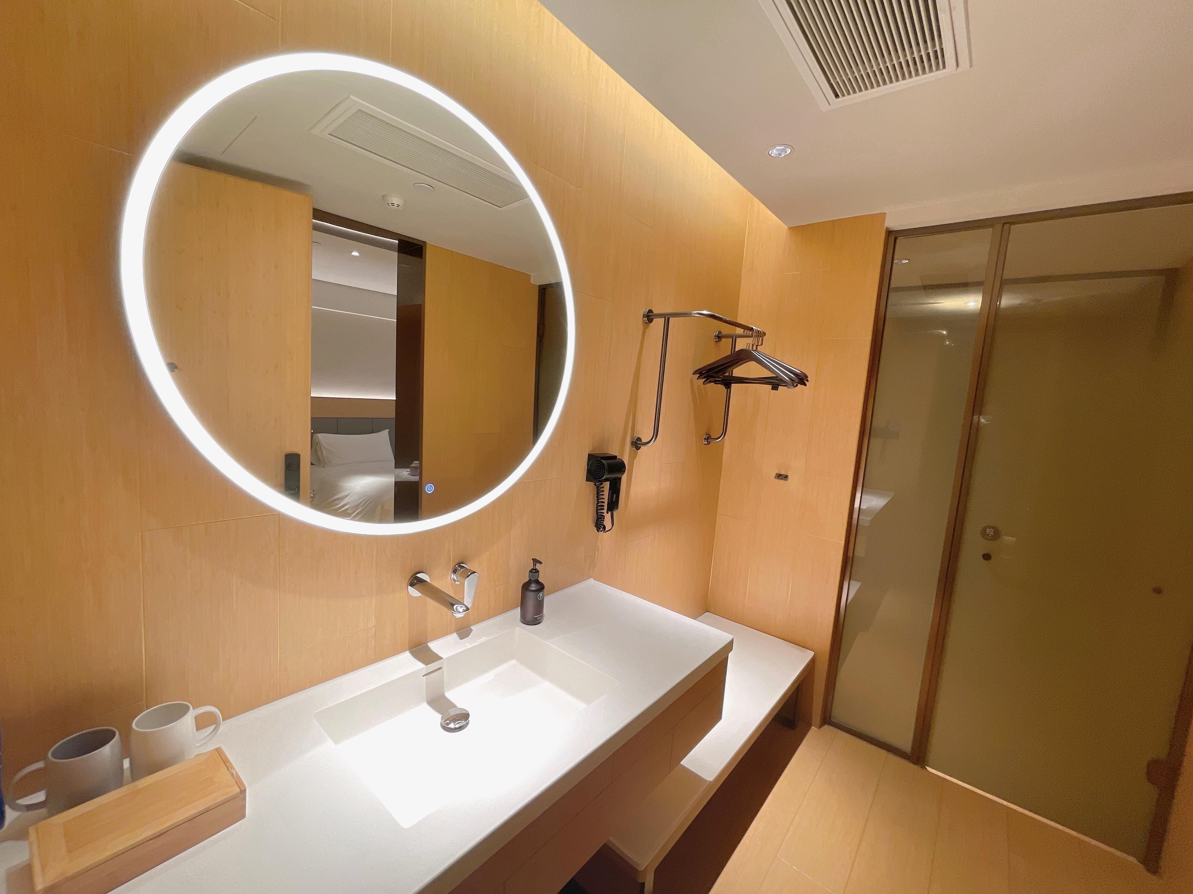Un bany modern amb un mirall gran, un lavabo blanc, un penjador de tovalloles i una zona de dutxa.