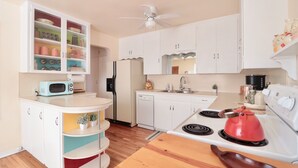 A compact kitchen with white cabinets, a microwave, a stove, and a ceiling fan.