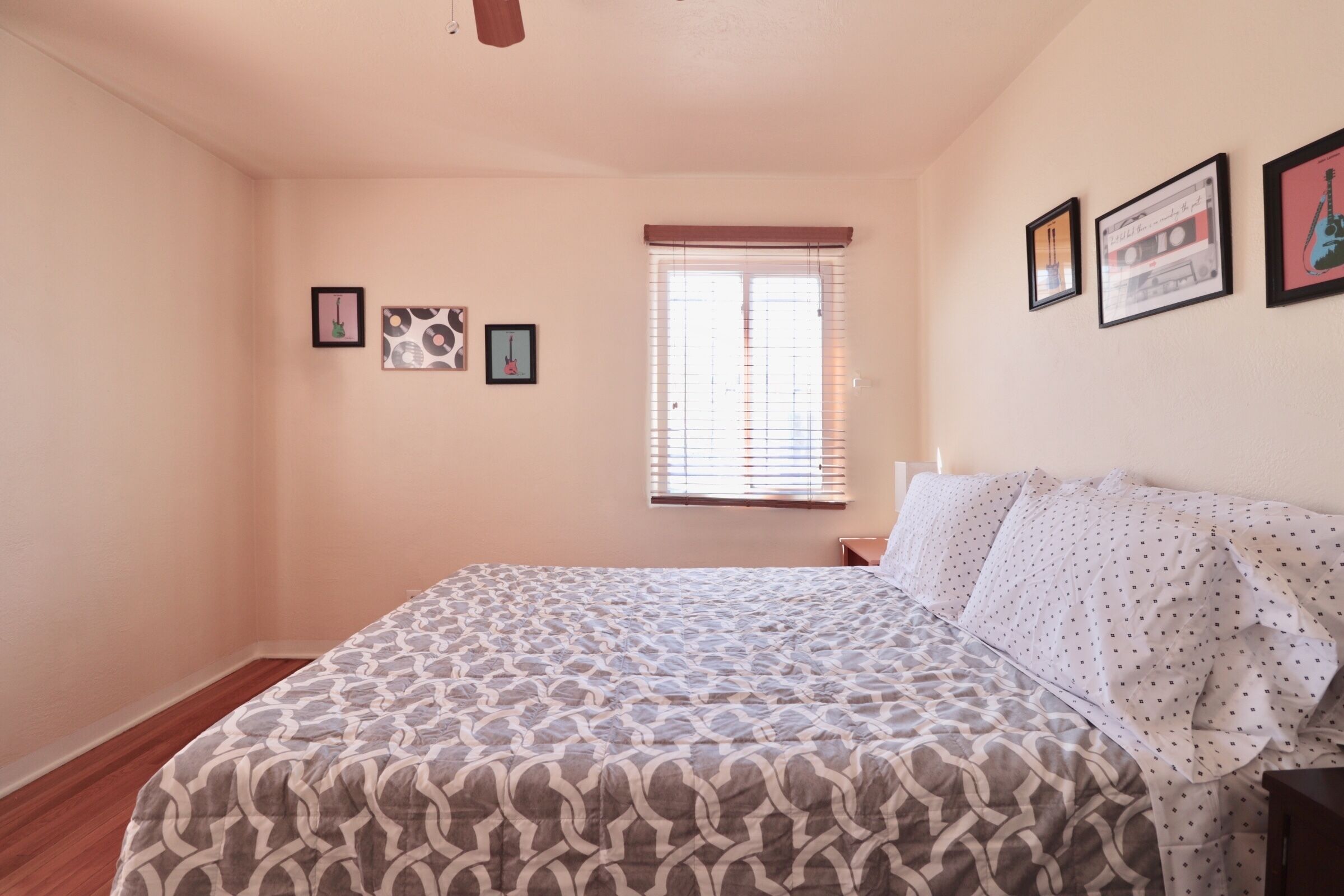Une chambre avec une couvre-lit à motifs, une fenêtre avec des stores et des tableaux encadrés accrochés au mur.