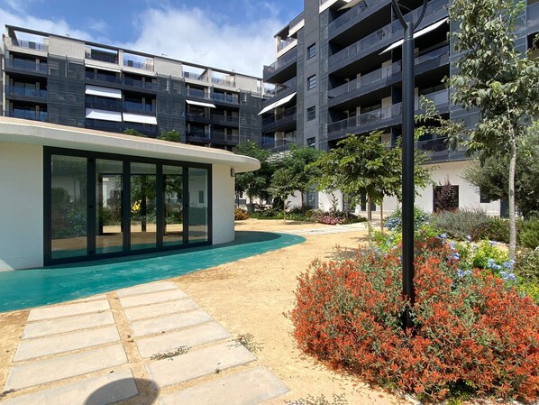 A modern building with a glass facade, a small pool, and a landscaped garden with colorful flowers.