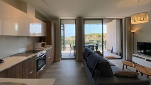 Cocina moderna con microondas, horno y pileta integrados. Cuenta con una zona de comedor con mesa y sillas, además de un sofá. La habitación tiene ventanas amplias y un balcón con vista al paisaje.
