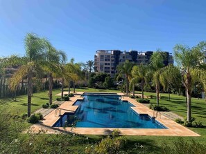 A rectangular swimming pool with a clear blue water surface, surrounded by a well-maintained lawn and palm trees. - Appartment near the sea  (La Vila Joiosa)