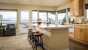 Una cocina con una isla grande, taburetes de bar, armarios de madera y vista al agua.