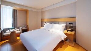 Een hotelkamer met een groot bed, nachtkastjes, een zithoek met een tafel en een raam met gordijnen.