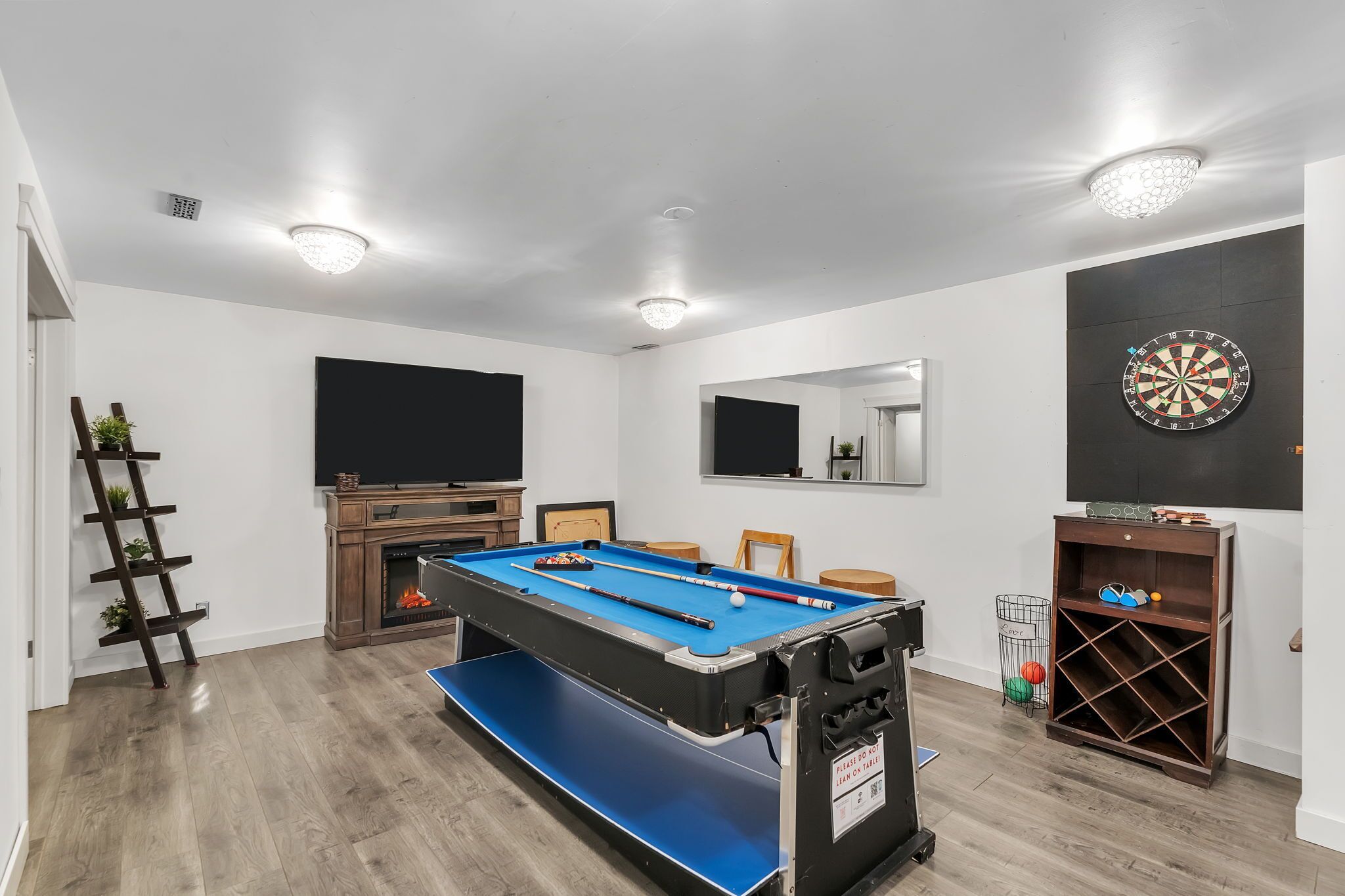A pool table with a blue felt surface, a dartboard, and a fireplace.
