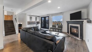 A modern living room with a black leather sofa, a fireplace, and a television mounted on the wall.