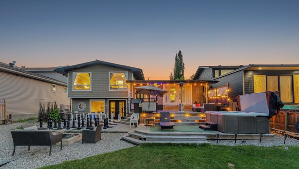A modern two-story house with a deck, outdoor seating, and a large TV.