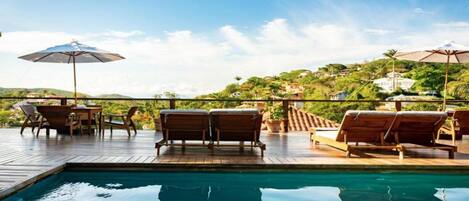 A poolside area with lounge chairs and umbrellas, overlooking a hillside with buildings.