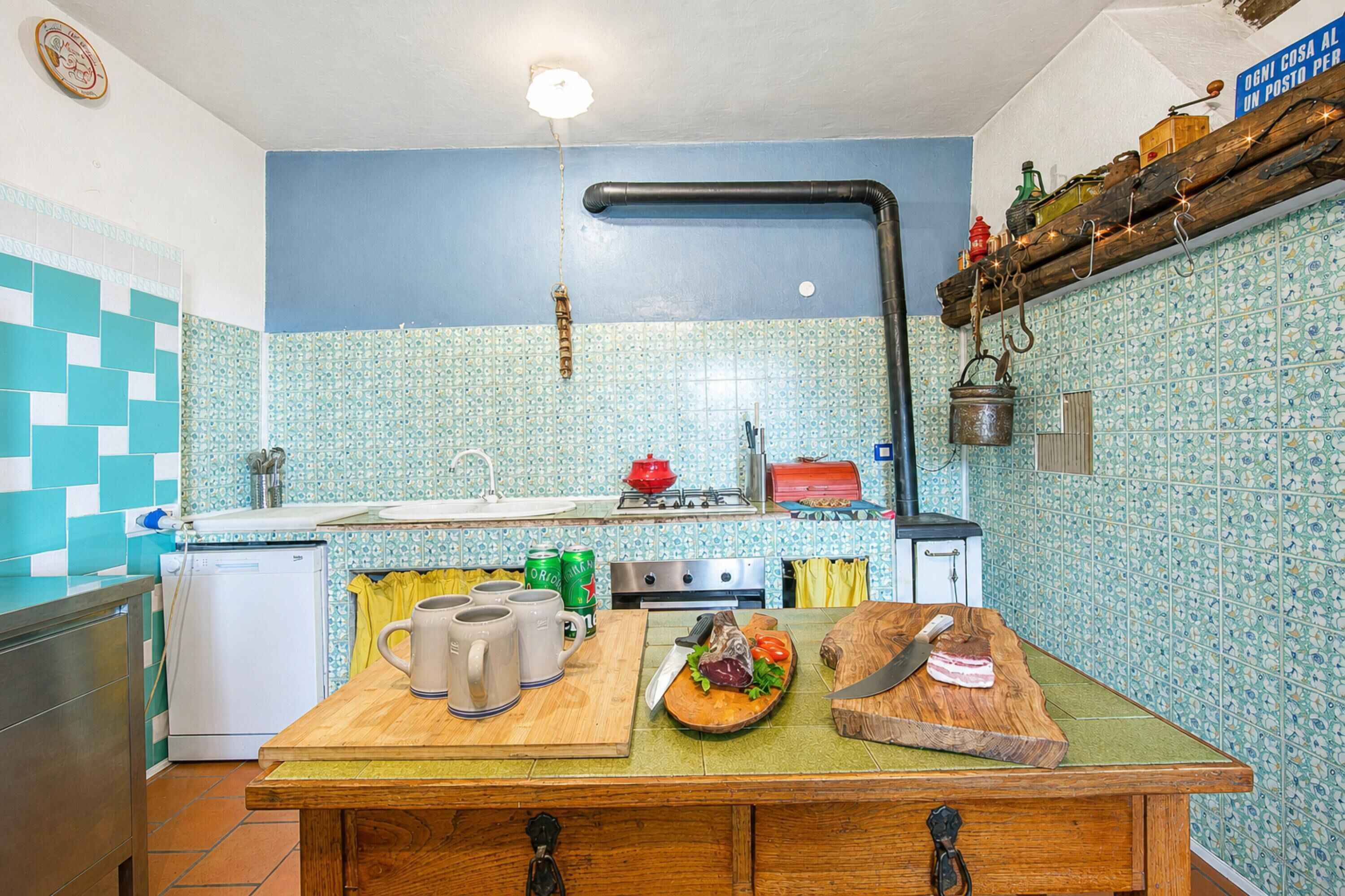 Una cocina con salpicadero de azulejos, una mesa de madera, un fregadero, una estufa y diversos utensilios de cocina.