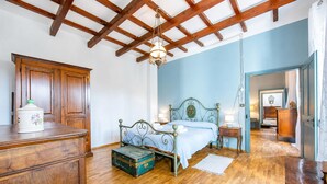 Une chambre avec un lit en bois, une commode, un coffre vert et un plafond en bois.