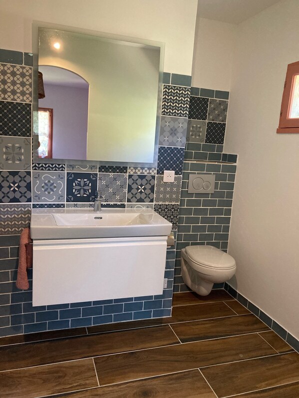Un baño con lavamanos blanco, toallero, inodoro y espejo. Las paredes están revestidas con diversos diseños.