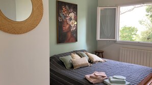 Une chambre à coucher avec un lit, des oreillers, un tableau, un miroir et une fenêtre.